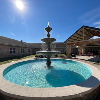 A serene outdoor space featuring a beautiful fountain surrounded by a sparkling pool under the bright sun.