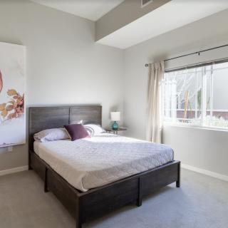 A modern, minimalist bedroom with a large bed and natural light from a window.
