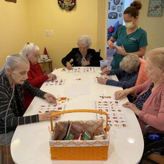 A group of elderly individuals engaged in an activity at a table, with a caregiver nearby.