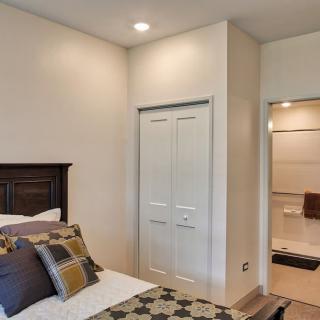 A cozy bedroom with a neatly made bed, accented with patterned pillows and a view of the closet and adjacent room.