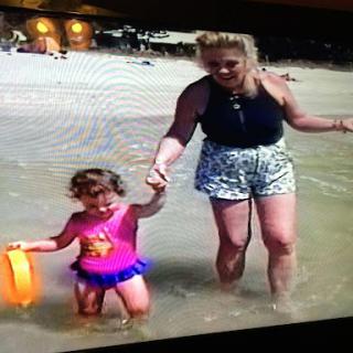 A joyful moment at the beach, where a mother is walking hand-in-hand with her young daughter as they play in the water.