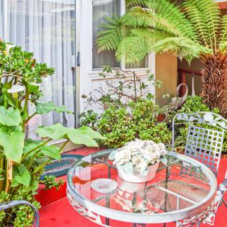 A cozy outdoor patio with a glass table and chairs surrounded by lush greenery.