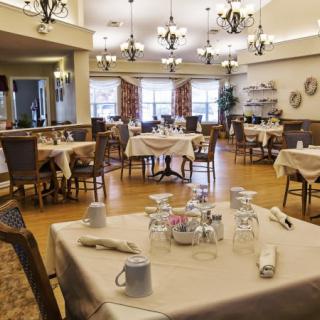 A well-decorated dining area with neatly arranged tables and chairs, illuminated by elegant chandeliers.