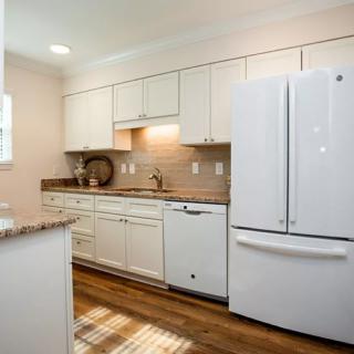 A modern kitchen with white cabinetry and appliances, featuring a wooden floor.