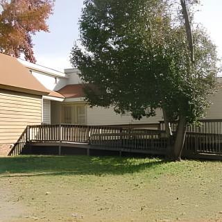 A house with a wooden deck and surrounding trees and lawn.