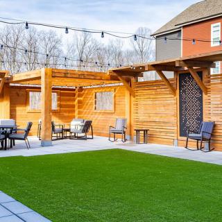 A cozy outdoor patio area with a pergola, featuring artificial grass and comfortable seating.