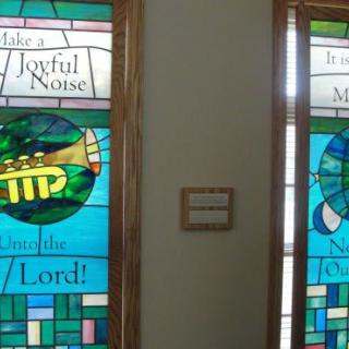 Stained glass windows featuring a trumpet with religious inscriptions.