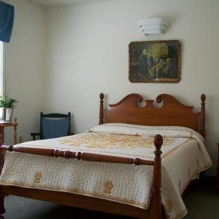 A cozy bedroom with a wooden bed, decorative quilt, and wall art.