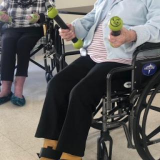 Seniors participating in a fitness class using small weights from their wheelchairs.
