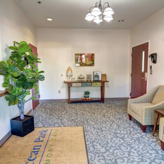 A welcoming lobby area with a comfortable armchair, potted plant, and a console table under a mirror.