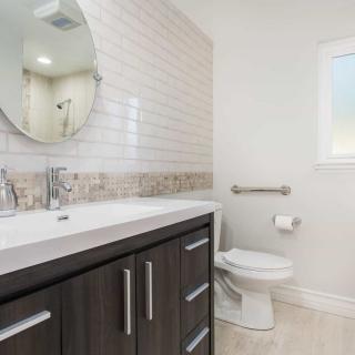 A modern bathroom featuring a sink with a dark cabinet, round mirror, and tiled backsplash.