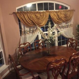 A cozy dining room with an elegant wooden table and chairs, adorned with ornate curtains and a floral centerpiece.