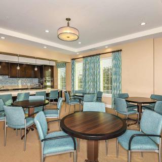 A well-lit dining area with round tables, cushioned chairs, and decorative curtains.