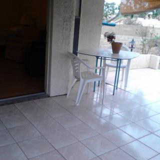 An outdoor patio with a table, a white chair, and a potted plant on a tiled floor.