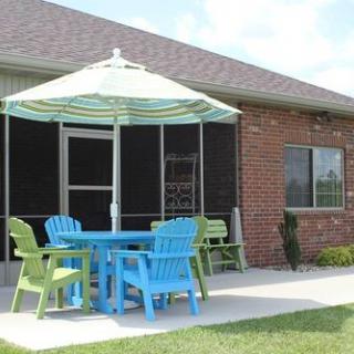 A patio with colorful chairs and a table under a striped umbrella next to a brick house.