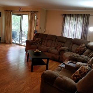 A cozy living room with a sectional sofa, hardwood floors, and a sliding glass door leading to an outdoor area.