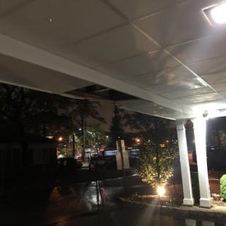 A nighttime view of a well-lit outdoor area with an illuminated ceiling and surrounding greenery.