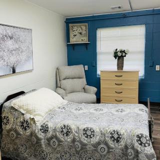 A cozy bedroom featuring a neatly made bed, a comfortable chair, and a stylish dresser against a blue wall.