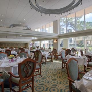 An elegant dining room with tables and chairs, featuring large windows allowing natural light to fill the space.