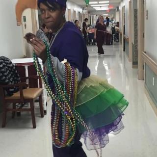 A person dressed in a whimsical costume with colorful beads, standing in a hospital hallway.