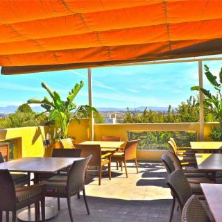 A sunny outdoor restaurant patio with tables, chairs, and a scenic view.