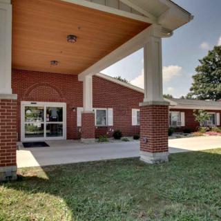 A brick building entrance with columns and a landscaped lawn.