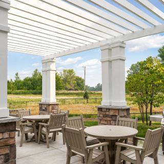 A serene outdoor seating area with tables and chairs under a pergola, surrounded by nature.