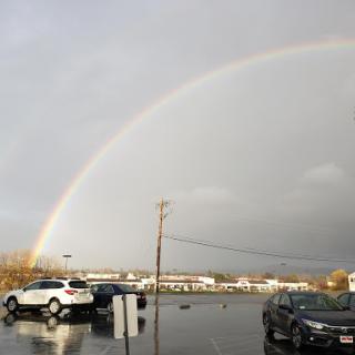 A beautiful rainbow stretches across the sky after a rain shower, illuminating a parking lot.