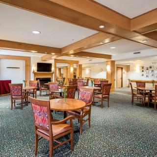A cozy dining area with wooden beams, tables, and chairs arranged on a carpeted floor.