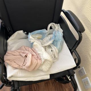 A wheelchair with clothing and a bag placed on its seat indoors.