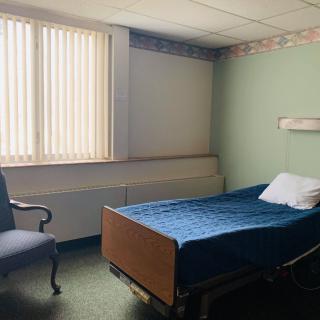 An empty hospital room with a bed and a chair by the window.
