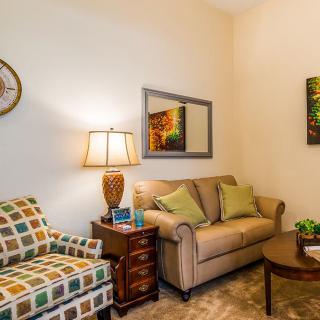 A cozy living room with a sofa, armchair, lamp, and colorful wall art.