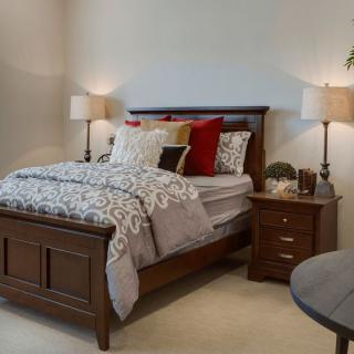 A cozy bedroom with a wooden bed and matching nightstands, adorned with decorative pillows and table lamps.