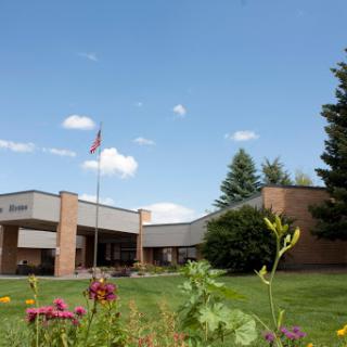 A school building with a flagpole, surrounded by flowers and trees under a clear blue sky.