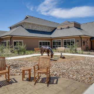 A peaceful outdoor seating area with wooden chairs and a statue in front of a modern building.