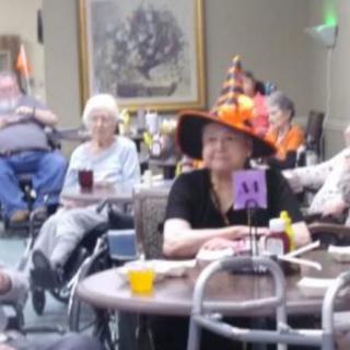 A group of seniors celebrating Halloween in a nursing home, with decorations and festive hats.