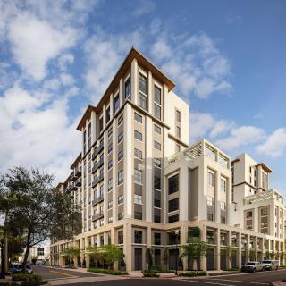 A modern urban building with a clear blue sky and surrounding trees.