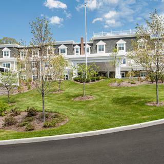 A large multi-story building surrounded by a well-maintained lawn and trees under a clear blue sky.