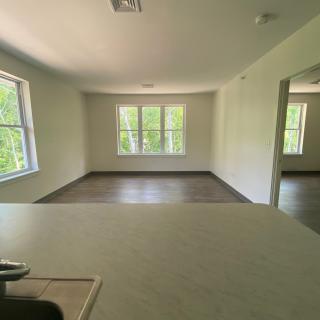An empty apartment living area with large windows and hardwood flooring, allowing for abundant natural light.