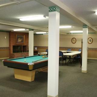 A recreation room featuring a pool table, tables, and chairs under bright lighting.