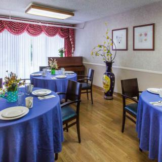 A dining room with tables covered in blue tablecloths, adorned with flower arrangements, and a piano in the background.