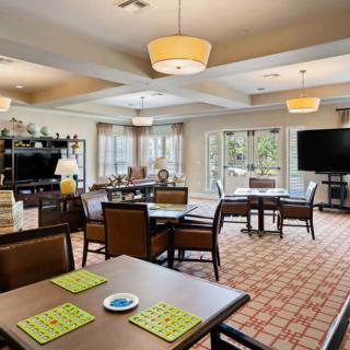 A spacious, well-lit living and dining area with multiple tables, comfortable seating, and large windows providing natural light.