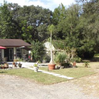 A small house with a patio, surrounded by a yard and trees.