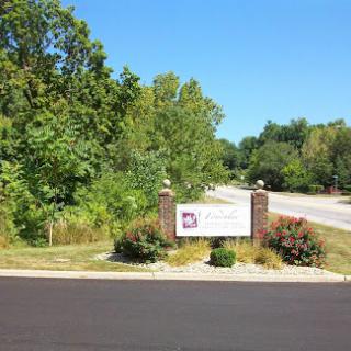 A scenic view featuring a sign at the edge of a road surrounded by lush greenery and a clear blue sky.