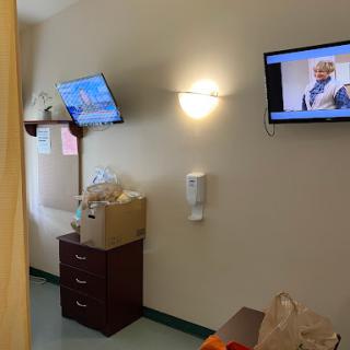 A view of a hospital room featuring two televisions and a dresser.