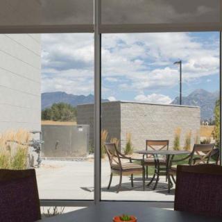 A scenic view of a patio with outdoor seating, framed by a window, showcasing mountains and a cloudy sky in the background.