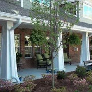 A cozy porch with seating, surrounded by plants and landscaping.