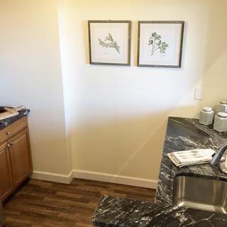 A kitchen corner featuring wooden cabinets, a marble countertop, and decorative artwork on the wall.