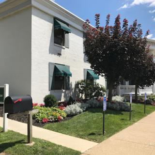 A well-maintained residential building surrounded by greenery and colorful flowers.
