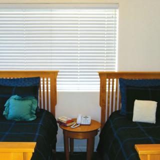 A cozy bedroom featuring twin beds with wooden headboards and a central nightstand under window blinds.